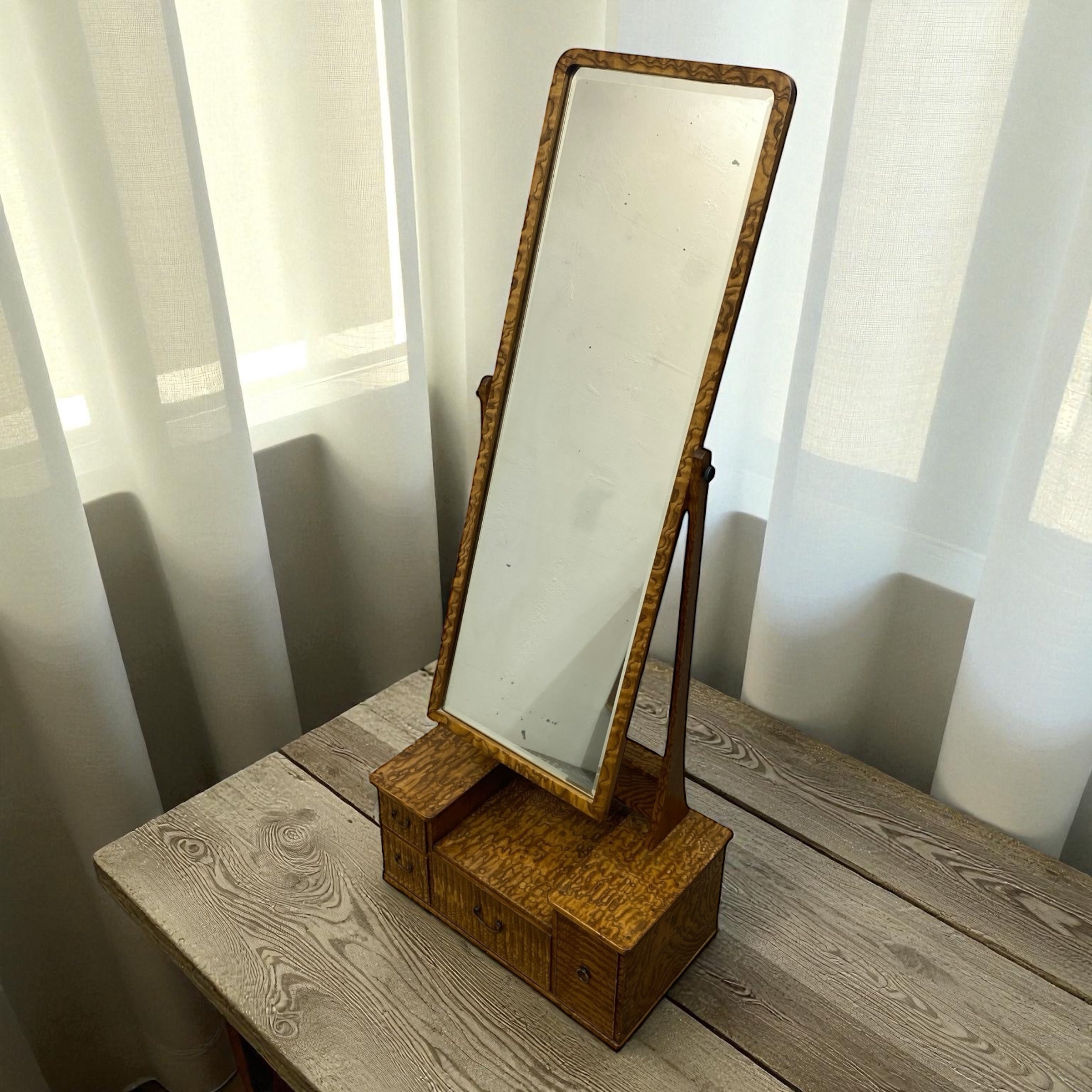 Wooden vanity mirror with stand on a wooden surface with white curtains in the background