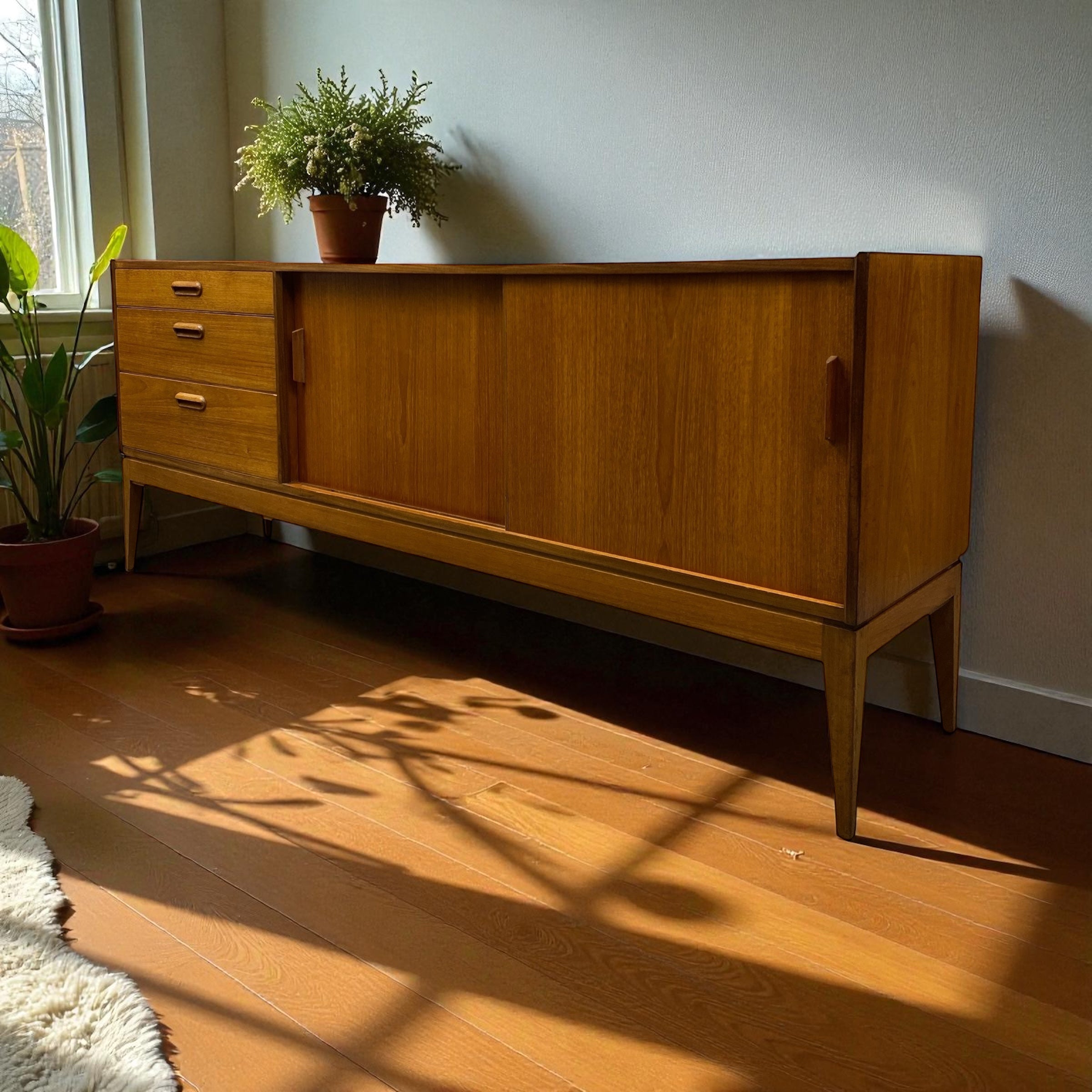 Wooden sideboard with a plant on top in a room with sunlight casting shadows.
