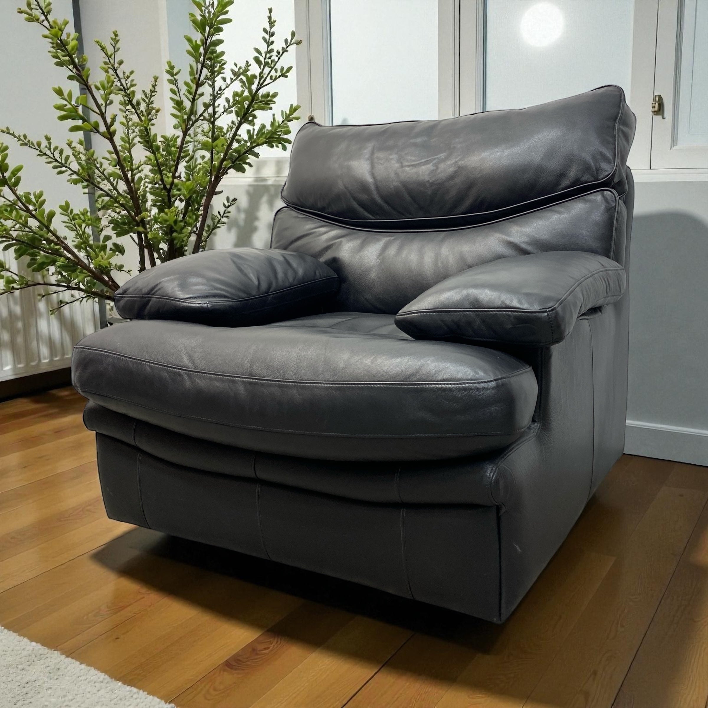 Gray leather armchair in a room with wooden floor and plant
