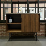 Load image into Gallery viewer, Wooden cabinet with a glass shelf against a brick wall
