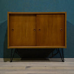 Load image into Gallery viewer, Wooden cabinet with black legs against a blue wall
