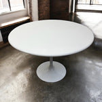 Load image into Gallery viewer, White round table with a pedestal base in a room with concrete flooring and large windows.
