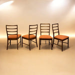 Load image into Gallery viewer, Four wooden chairs with orange cushions on a beige floor and wall.
