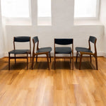 Load image into Gallery viewer, Four wooden chairs with black seats on a wooden floor.
