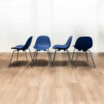 Load image into Gallery viewer, Four blue chairs lined up on a wooden floor with a white wall background
