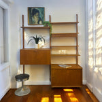 Load image into Gallery viewer, Wooden wall unit with shelves and a small table in a room with sunlight streaming in.
