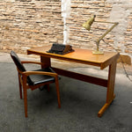 Load image into Gallery viewer, Wooden desk with a vintage typewriter and lamp against a stone wall.
