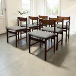 Load image into Gallery viewer, Set of six wooden chairs with gray cushions in a room with large windows.
