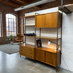 Load image into Gallery viewer, Wooden shelving unit with drawers and cabinets in a room with brick walls and large windows.
