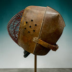 Load image into Gallery viewer, A vintage brown leather fencing mask with a wire cage face guard, mounted on a display stand against a blue-to-white gradient background.

