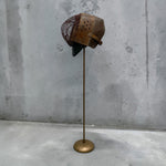 Load image into Gallery viewer, A vintage brown leather and wire fencing mask displayed on a brass stand against a textured gray concrete wall.
