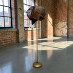 Load image into Gallery viewer, A vintage-style metal and wood birdhouse-shaped floor lamp with a brass stand, displayed in a sunlit industrial loft with brick walls and large windows.
