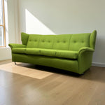 Load image into Gallery viewer, A bright lime green upholstered wingback sofa with button tufting on the backrest, shown in a minimalist room with light wood floors and a white wall.
