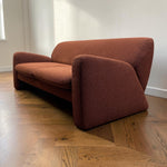 Load image into Gallery viewer, A mid-century modern loveseat sofa upholstered in a textured rust-orange fabric, set on a polished wooden parquet floor against a white wall.

