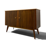 Load image into Gallery viewer, Mid-century modern wooden sideboard cabinet with two doors, vertical wood grain panels, brass-tone knobs, and tapered legs, shown on a white background with a soft shadow.

