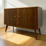 Load image into Gallery viewer, Mid-century modern wooden sideboard cabinet with two doors, round wooden knobs, and tapered legs, shown on a light wood floor against a white wall with natural sunlight.
