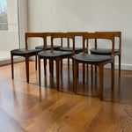 Load image into Gallery viewer, Six mid-century modern dining chairs with dark brown wood frames and black upholstered seats, arranged on a polished hardwood floor against a white wall.
