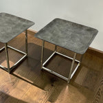 Load image into Gallery viewer, Two square nesting side tables with textured gray stone-look tops and polished silver metal frames, shown on a wooden floor against a plain wall.
