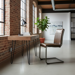 Load image into Gallery viewer, A modern workspace setup in a loft-style room with exposed brick walls and large windows. The setup includes a light oak wood desk with black hairpin legs, a black desk lamp, a green potted plant, and a brown leather upholstered chair with a curved metal frame.
