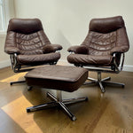 Load image into Gallery viewer, A mid-century modern two-piece lounge set featuring two matching brown leather swivel chairs and an ottoman, supported by chrome star bases, set on a wooden floor against a plain wall.
