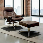Load image into Gallery viewer, A brown leather recliner chair with an attached matching ottoman, both with chrome star base legs, placed on a light rug in a modern loft-style room with brick columns and large windows.
