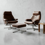 Load image into Gallery viewer, Two brown leather lounge chairs with matching ottomans and chrome swivel bases, arranged in a minimalist studio setting with a small wooden side table.
