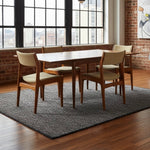 Load image into Gallery viewer, A mid-century modern dining set consisting of a rectangular wooden table and four matching chairs with beige upholstered seats, shown on a gray rug in a loft-style room with brick walls and large windows.
