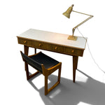 Load image into Gallery viewer, A mid-century modern writing desk with a white top, brown wood frame, and matching chair, accompanied by a brass desk lamp, shown on a white background with a prominent shadow.
