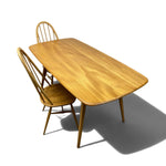 Load image into Gallery viewer, A mid-century modern wooden dining table with a warm honey finish and two matching spindle-back chairs, shown on a clean white background with a soft shadow.
