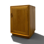 Load image into Gallery viewer, A mid-century modern wooden cabinet with a warm honey-toned finish, featuring a single door with a recessed panel design and a round pull handle, shown on a white background with a soft shadow.

