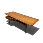 Load image into Gallery viewer, A mid-century modern wooden writing desk with a warm medium-brown finish, featuring a single drawer on the left side and a lower shelf, shown on a white background with a soft shadow.
