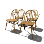 Load image into Gallery viewer, Four wooden dining chairs with spindle backs and tapered legs, arranged in a group on a white background with cast shadows.
