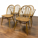 Load image into Gallery viewer, Four wooden spindle-back dining chairs with a warm honey finish, arranged on a dark wood floor against a plain white wall.
