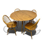 Load image into Gallery viewer, A round wooden dining table with four matching spindle-back chairs, shown on a plain white background with soft shadows.
