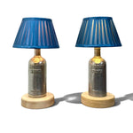 Load image into Gallery viewer, A pair of table lamps made from repurposed Absolut Vodka bottles, featuring blue pleated fabric shades, clear glass bodies, and round light wood bases, set against a plain white background.
