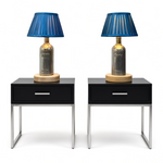 Load image into Gallery viewer, Two matching modern nightstands with black tops, single front drawers, and slim silver metal legs, each holding a table lamp with a blue pleated shade, a metallic bottle-shaped base, and a round light wood base.
