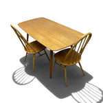Load image into Gallery viewer, A light oak wood dining table with two matching spindle-back chairs, shown from an elevated angle on a white background with a soft shadow.
