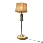 Load image into Gallery viewer, A vintage-style table lamp with a pleated beige fabric shade, a silver metal neck, a round wooden base, and a slim silver stem, shown lit against a white background with a soft shadow.
