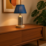 Load image into Gallery viewer, A table lamp styled on a wooden sideboard in a warm room setting, featuring a blue pleated shade and a metallic silver bottle-shaped base with 'Absolut Vodka' embossed on it.
