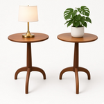 Load image into Gallery viewer, Two round wooden side tables with curved tripod-style legs, shown on a clean white studio background. One table holds a lit table lamp with a white drum shade and gold base, and the other holds a green potted plant in a white pot.
