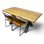 Load image into Gallery viewer, A live-edge wood dining table with a natural oak top and dark metal A-frame legs, accompanied by two modern chairs with light wood seats and black metal frames, shown on a white background.
