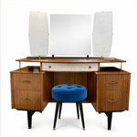 Load image into Gallery viewer, Mid-century modern wooden dressing table with a three-panel mirror, drawers, and a blue tufted velvet stool on a white background.
