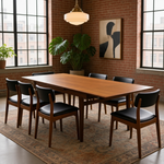 Load image into Gallery viewer, A mid-century modern dining room set featuring a rectangular wooden table and six matching chairs with black leather seats, arranged on a patterned area rug in a brick-walled room with large windows.
