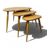 Load image into Gallery viewer, Three nested oval nesting tables in a light natural wood finish with tapered legs, shown on a white background with a soft shadow.
