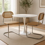 Load image into Gallery viewer, A round white marble-top dining table with a white tulip base, paired with two modern chairs featuring woven tan seats and backs and chrome cantilever frames, set on a beige rug in a bright room.
