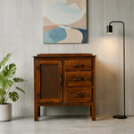 Load image into Gallery viewer, A rustic dark brown wooden sideboard cabinet with a door and three drawers, styled in a modern room setting with a potted plant, a black floor lamp, and an abstract painting on a light gray wood-paneled wall.
