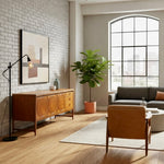 Load image into Gallery viewer, A modern living room scene featuring a mid-century wooden sideboard with circular details, a black floor lamp, a large potted fiddle-leaf fig, a gray sofa, and a tan leather armchair in front of a large arched window.
