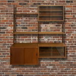 Load image into Gallery viewer, Mid-century modern wall-mounted wooden shelving and cabinet unit with glass-front upper cabinet and lower storage compartments, set against a red brick wall.
